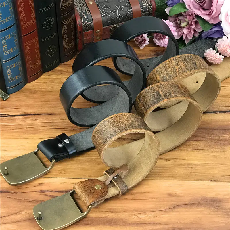 A collection of vintage-style black and tan genuine leather men jeans belts featuring brass owl buckles with a worn, distressed finish.