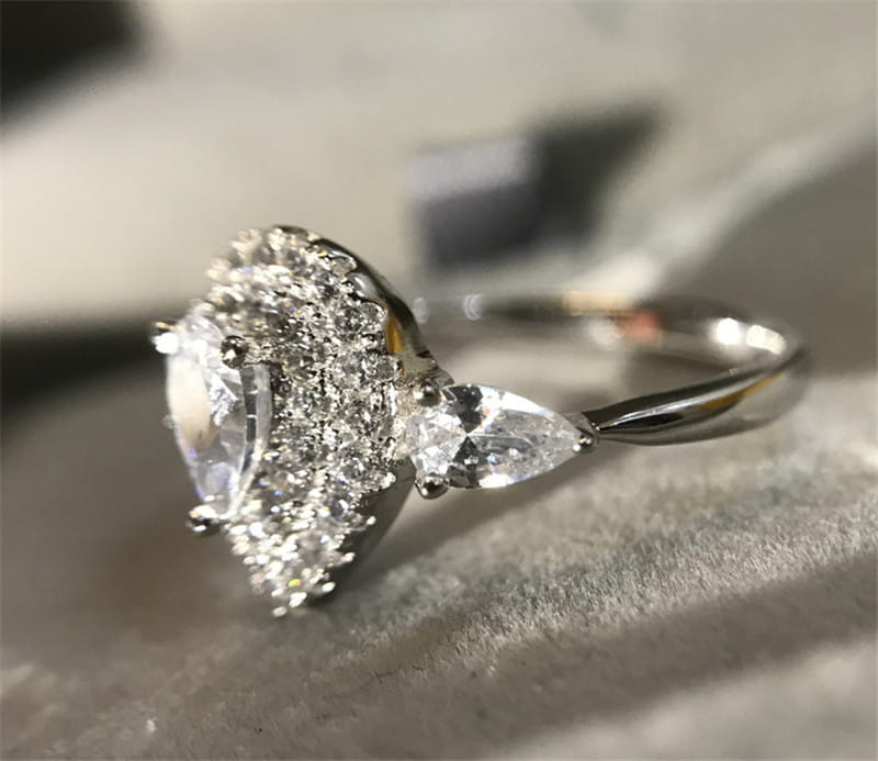 Bague de fiançailles en zircon goutte de larme rose étincelante à tons argentés, présentant un diamant central en forme de poire entouré d’un halo de diamants plus petits et rehaussé de pierres taillées en marquise.