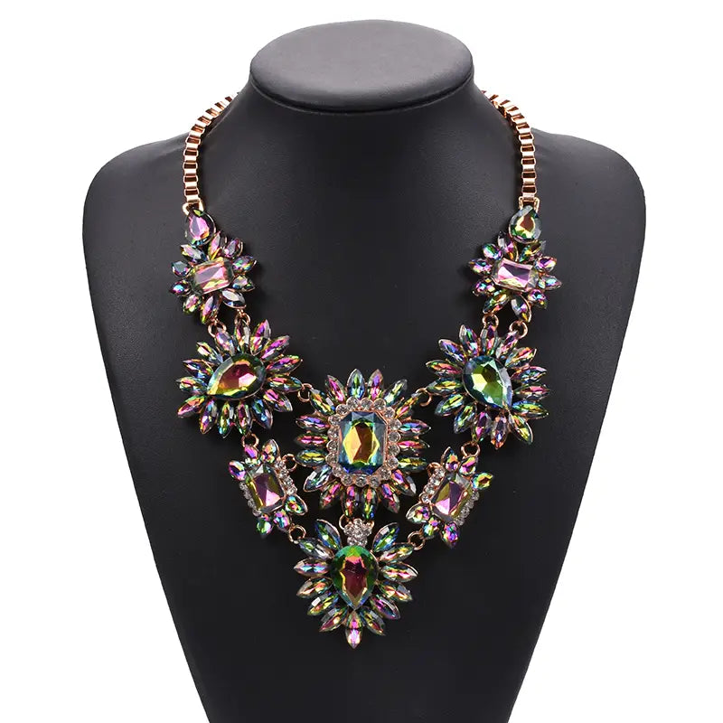 Un ras-du-cou bohème vibrant et multicolore en forme de collier-sautoir, en cristal, avec un fermoir ornemental et des cristaux arc-en-ciel irisés disposés en motifs floraux sur une chaîne à tons or rose.