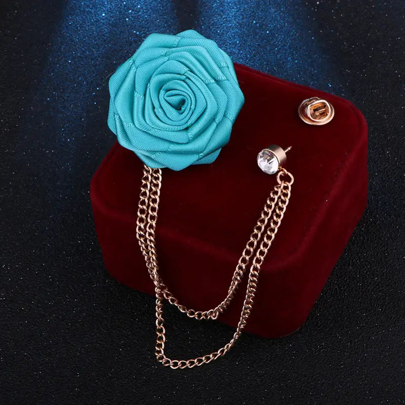 A turquoise fabric rose brooch with a gold-toned tassel chain and clasp designed as a men suit pin.