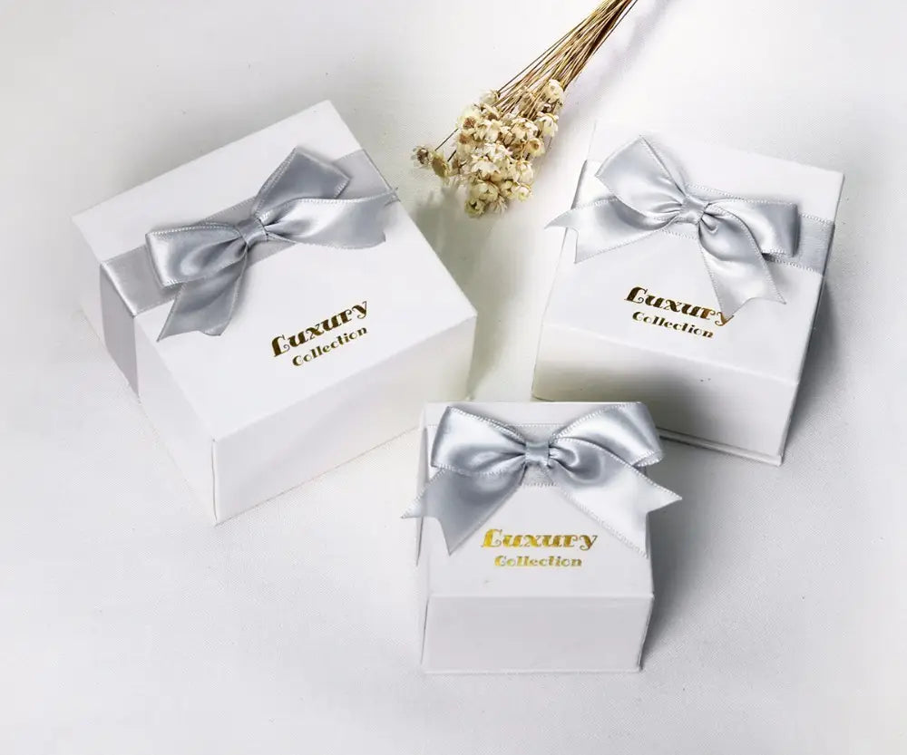 White square gift boxes with shiny silver satin bows and gold luxury collection lettering for Black and White Crystal Statement Flower Ring packaging.
