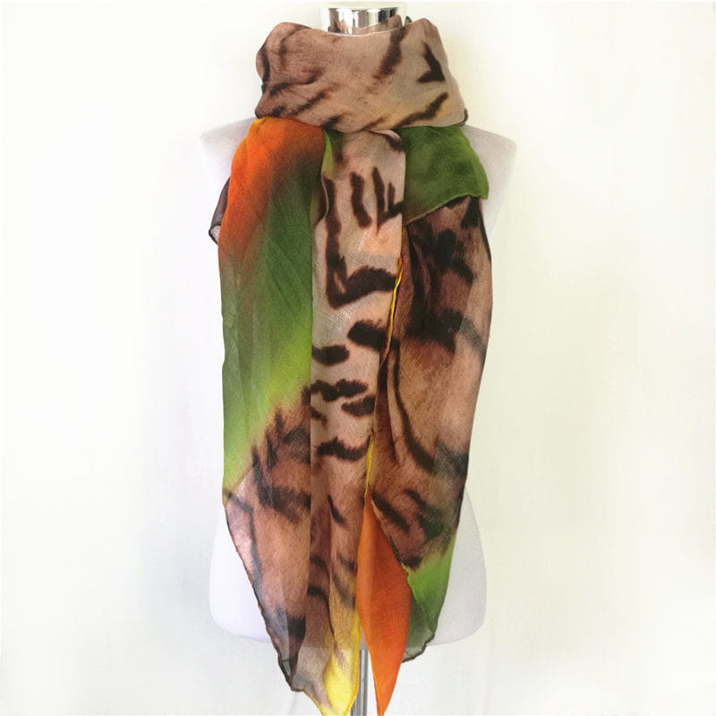 Una bufanda-capa de visón con flecos de leopardo, en un material translúcido y vibrante, con un patrón de rayas de tigre audaz en marrones y negros terrosos, acentuado por bordes con degradado vivo de naranja y verde.