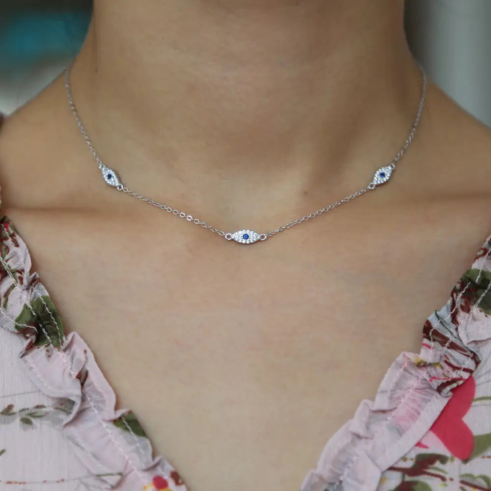 Silver evil eye charm necklace featuring a silver chain with three charms each having a central blue stone and surrounding clear cz crystals.