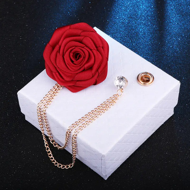 A vibrant red fabric rose flower brooch with a gold-toned tassel chain and crystal accent designed as an elegant men suit lapel pin.
