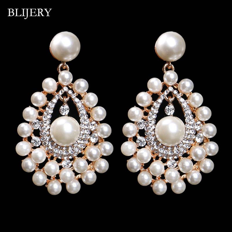 雫型の白いパールときらめくリ rhinestones をあしらった、ブライダル・クリスタル・シャンデリア・ジュエリーとしてのエレガントな真珠の雫型イヤリング。金色調のメタルにセットされた、装飾的な重ねの模様が特徴です。