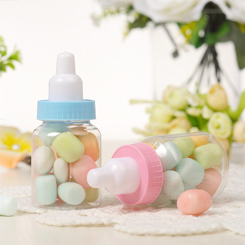 青とピンクのキャップを備えた透明なプラスチック製のベビーシャワー引き菓子用ミニミルクボトル。パステルカラーのキャンディを詰めています。