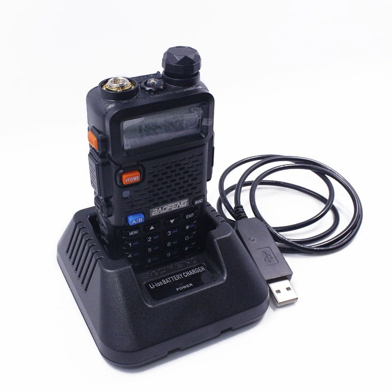 black baofeng uv-5r two-way radio with orange and blue buttons resting on its matching black li-ion battery charger for uv5r models.