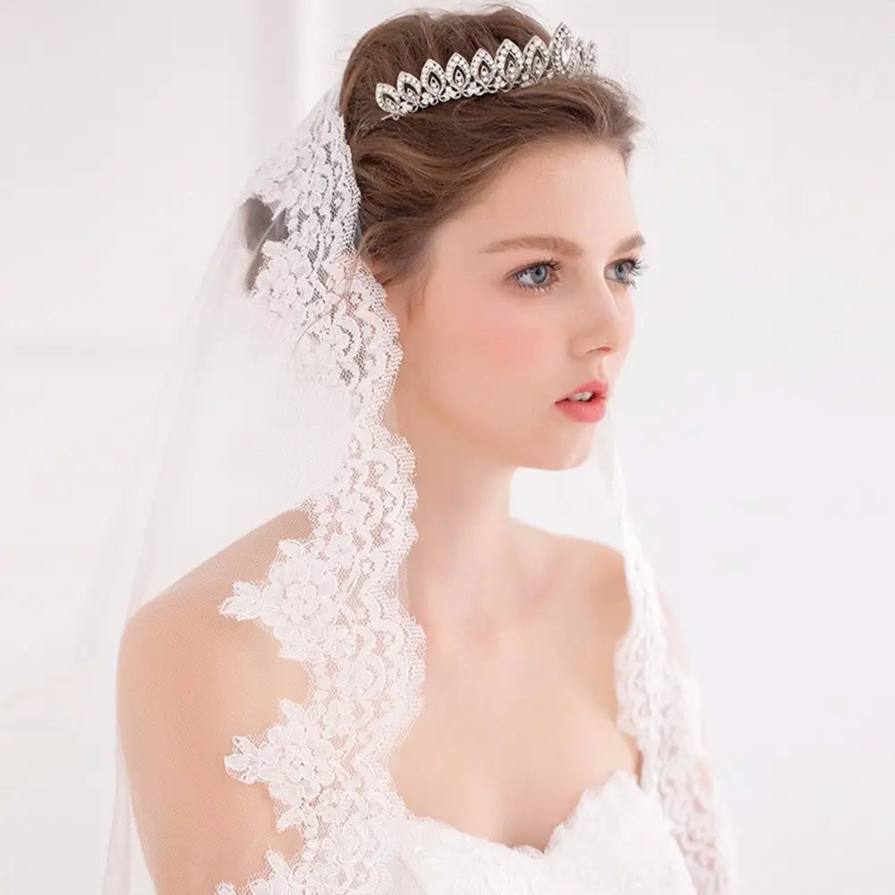 Una diadema de boda floral con tiara de novia delicada de cristal plateado, adornada con pedrería brillante y diseños intrincados con apariencia de hojas, que se lleva con elegancia sobre el cabello peinado de la novia.