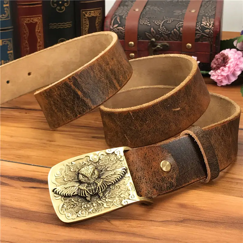 A vintage-style brown genuine leather men jeans belt featuring a brass owl belt buckle with an intricately engraved design.