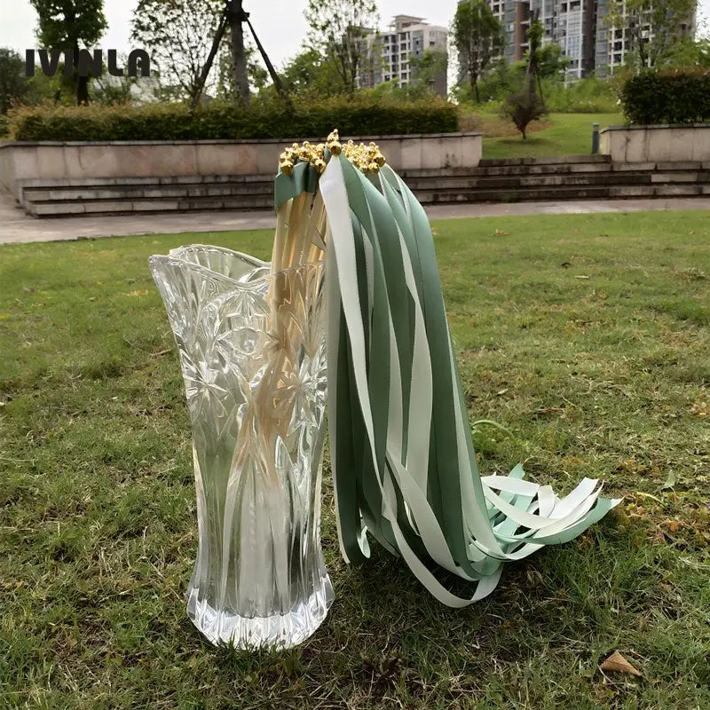 un vase en verre transparent à découpes complexes contenant des baguettes ruban de mariage vertes et blanches, avec des extrémités dorées, présenté en lot de 50.