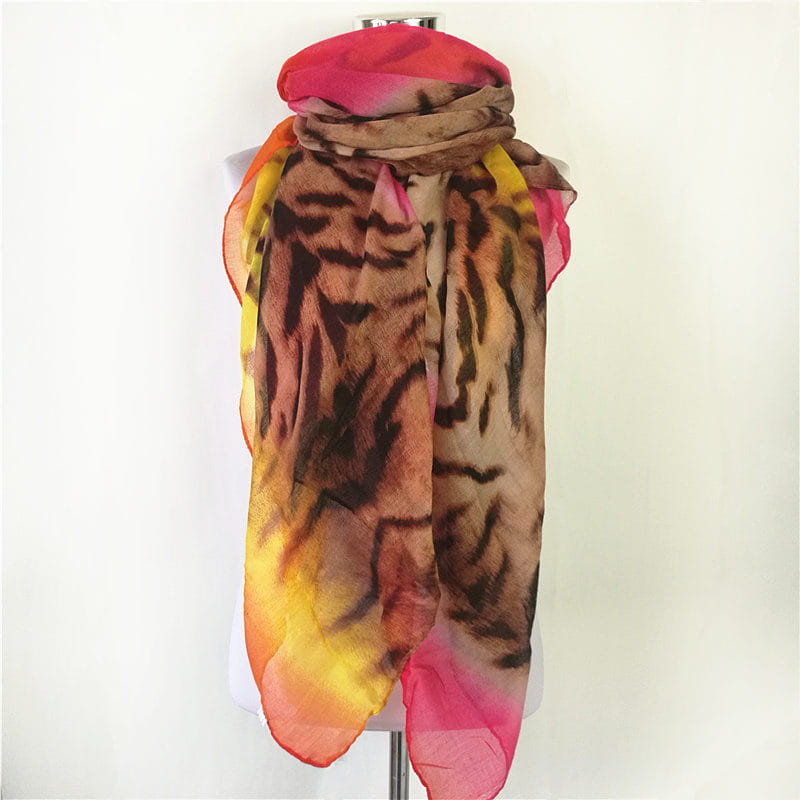 Una bufanda-capa de visón con flecos de leopardo vibrante, que presenta un estampado de tigre translúcido y audaz con bordes degradados en tonos de rosa, naranja, amarillo, marrón y negro.