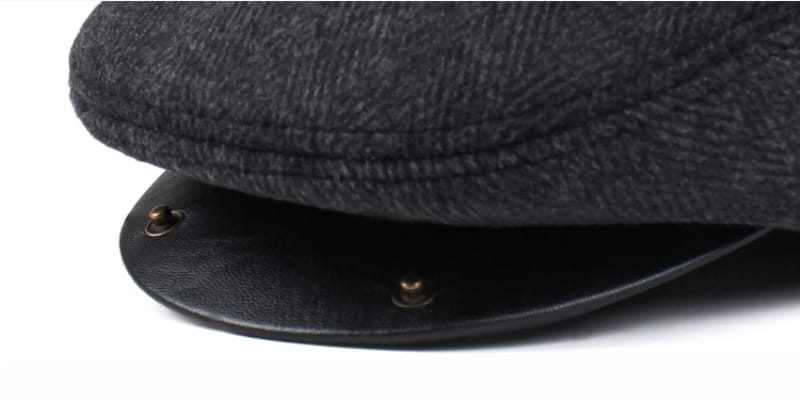 Boina de invierno para hombre tipo herringbone con cubreorejas, con lana negra texturizada y visera de cuero con remaches de latón.