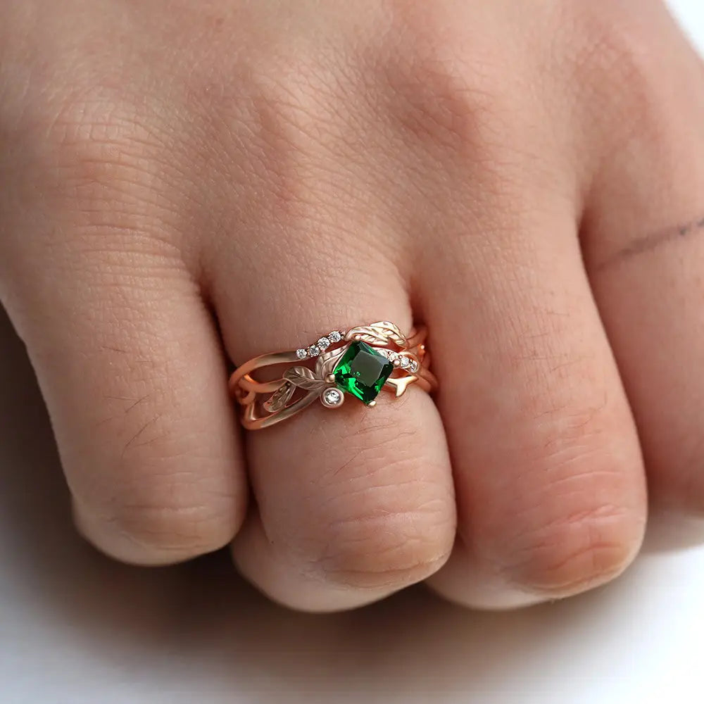 ダイヤモンドの葉のデザインアクセントを備えた、中央にエメラルドカットのグリーン宝石を配したローズゴールドのリング。