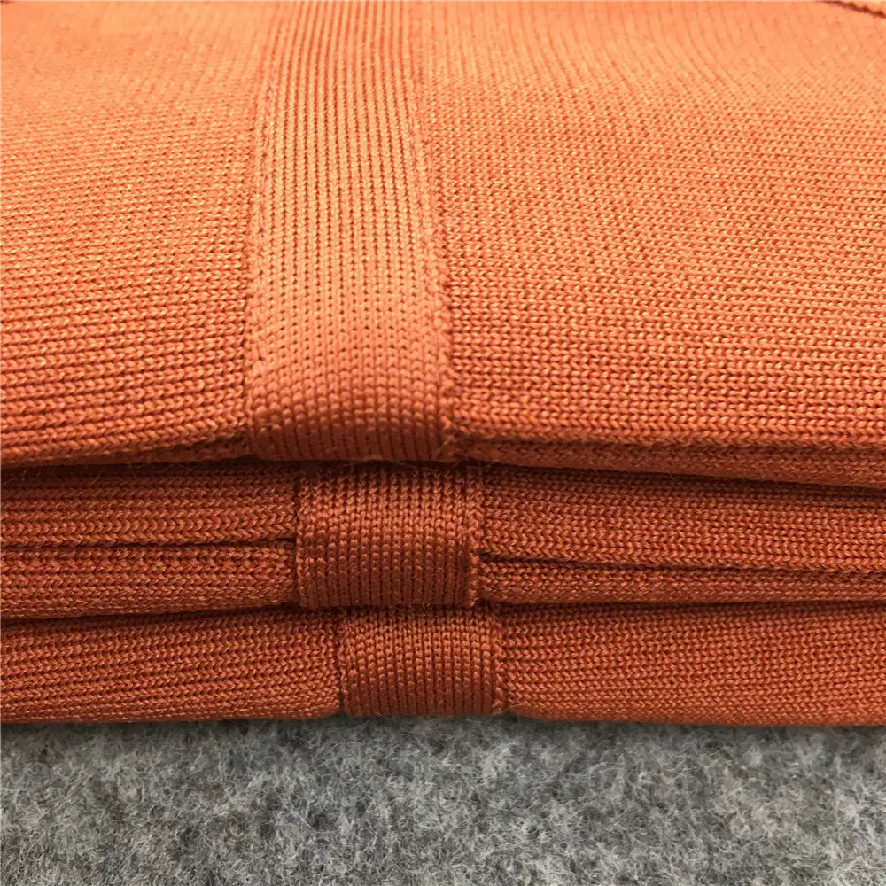Pièces de tissu tricoté orange empilées, texture côtelée et coutures renforcées pour une jupe midi bandeau pour femme à taille haute, style crayon.