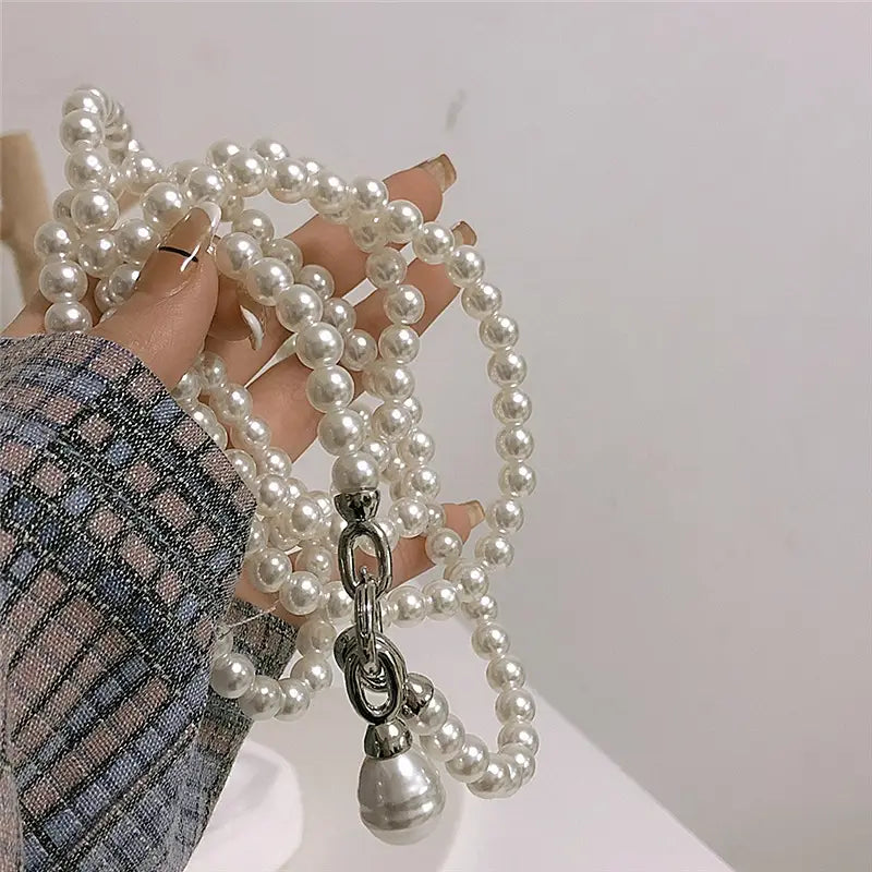 Un collier avec pendentif en forme de goutte de perle, présentant un délicat brin de perles blanches, une chaîne au ton argenté et un pendentif.