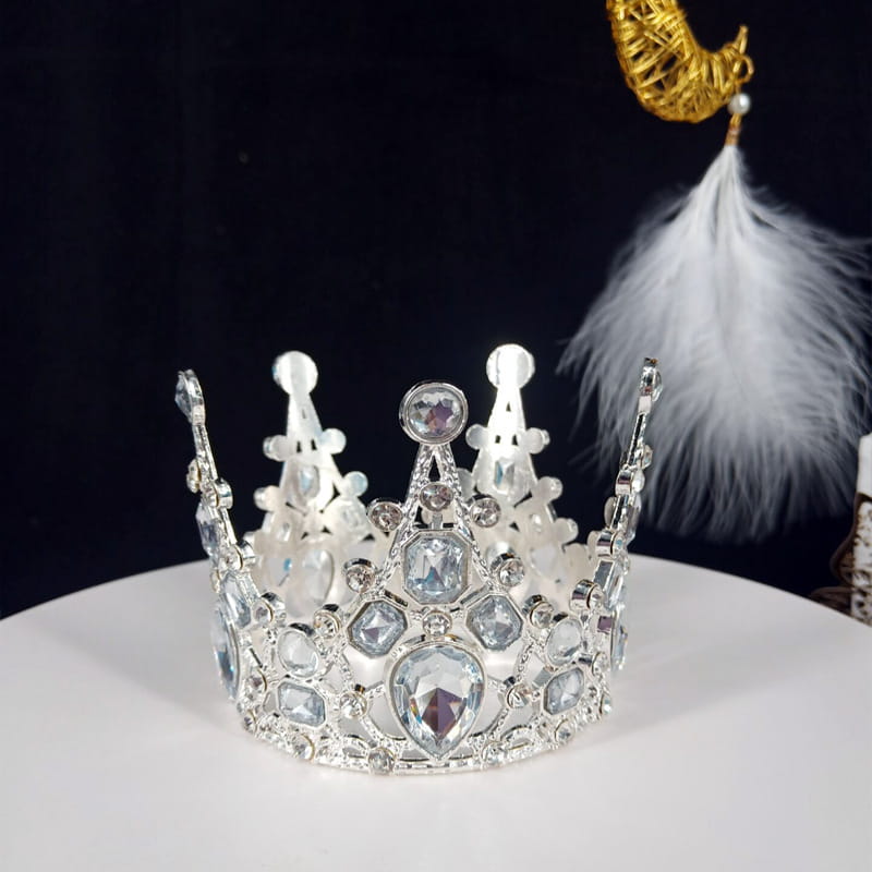 Ein funkelnder silberner Mini-Kronen-Tortenaufsatz und eine Haar-Tiara, verziert mit klaren und leicht violett schimmernden Kristallen mit detaillierten Filigran-Details.