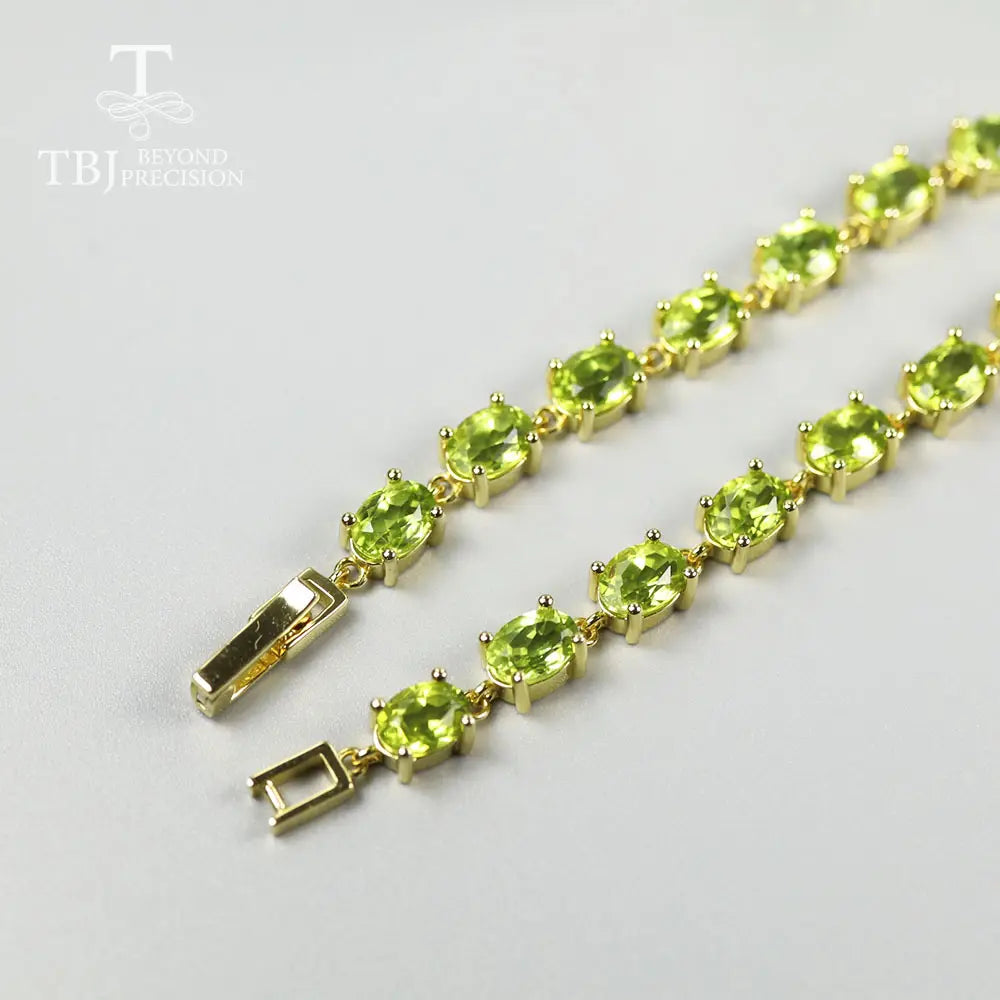 Una pulsera tipo tenis delicada de plata de ley en tono dorado, con una fila de vibrantes piedras ovaladas de peridoto, colocadas en engastes.