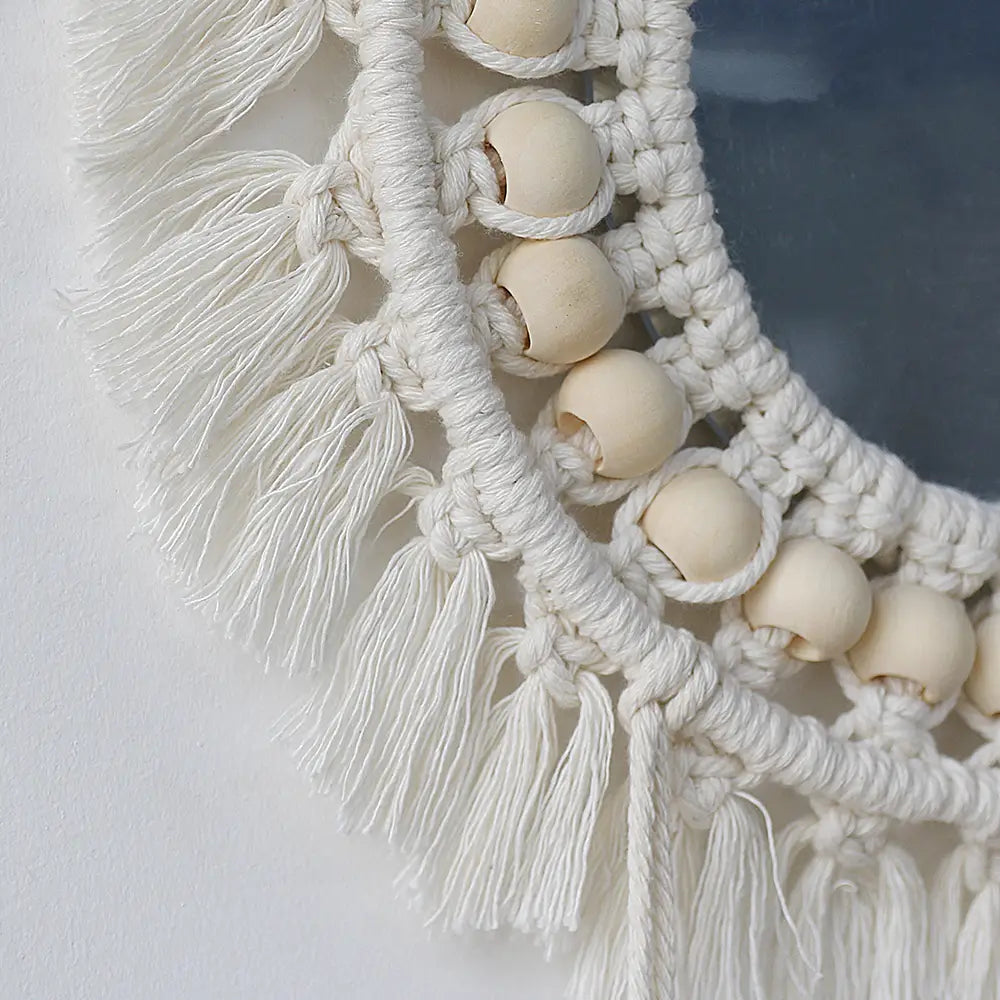 A white macrame wall mirror with wooden beads and fringe made of cotton for living room home decor.