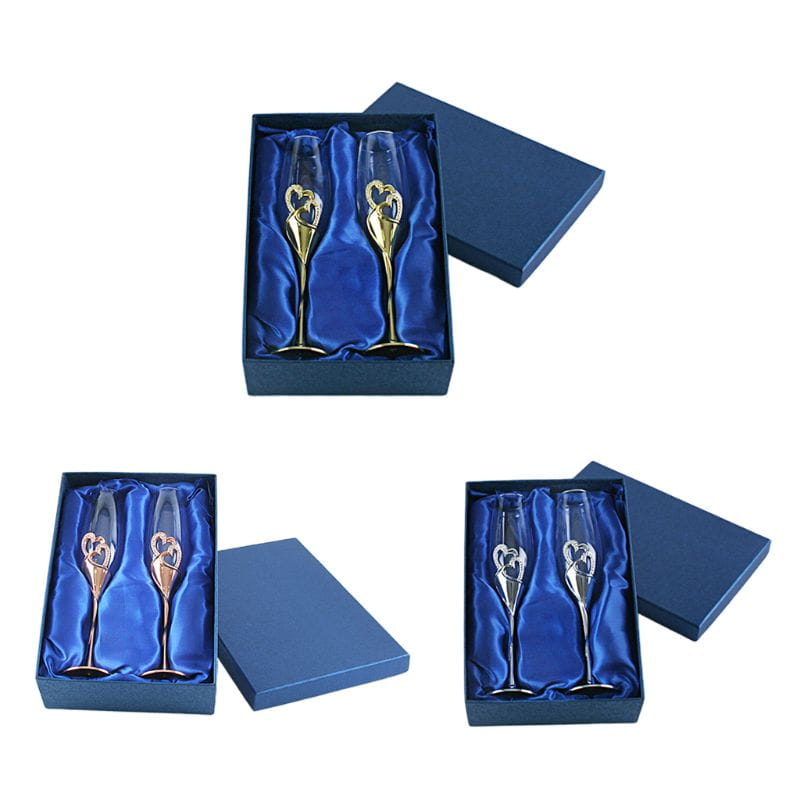 A pair of elegant wedding champagne flutes with gold-toned heart-shaped embellishments on the stems presented in a luxurious blue gift box.