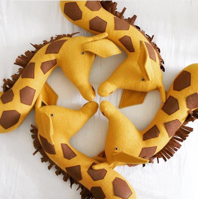 Eine gelbe Filz-3D-Cartoon-Tierkopf-Wanddekoration in Form einer Giraffe mit braunen sechseckigen Patches und gefransten Rändern.