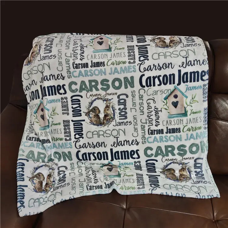 Eine weiche weiße, personalisierte Baby-Wickeldecke aus Fleece mit einem sich wiederholenden Muster der Namen carson james in verschiedenen Schriftarten und Farben, mit Illustrationen von Vogelhäusern und Kaninchen
