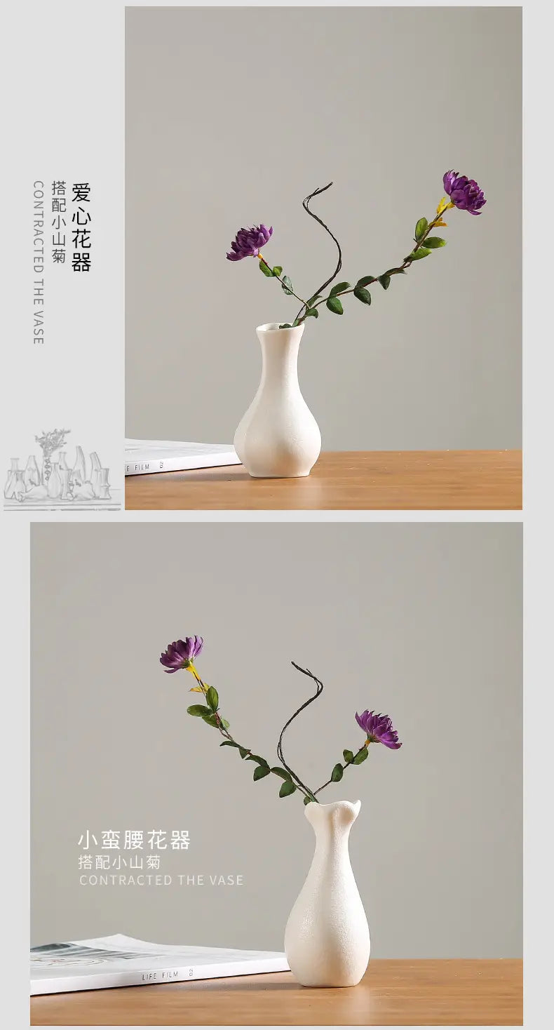 A modern white ceramic vase with a slender neck and rounded body holding two purple flowers for floral decor.