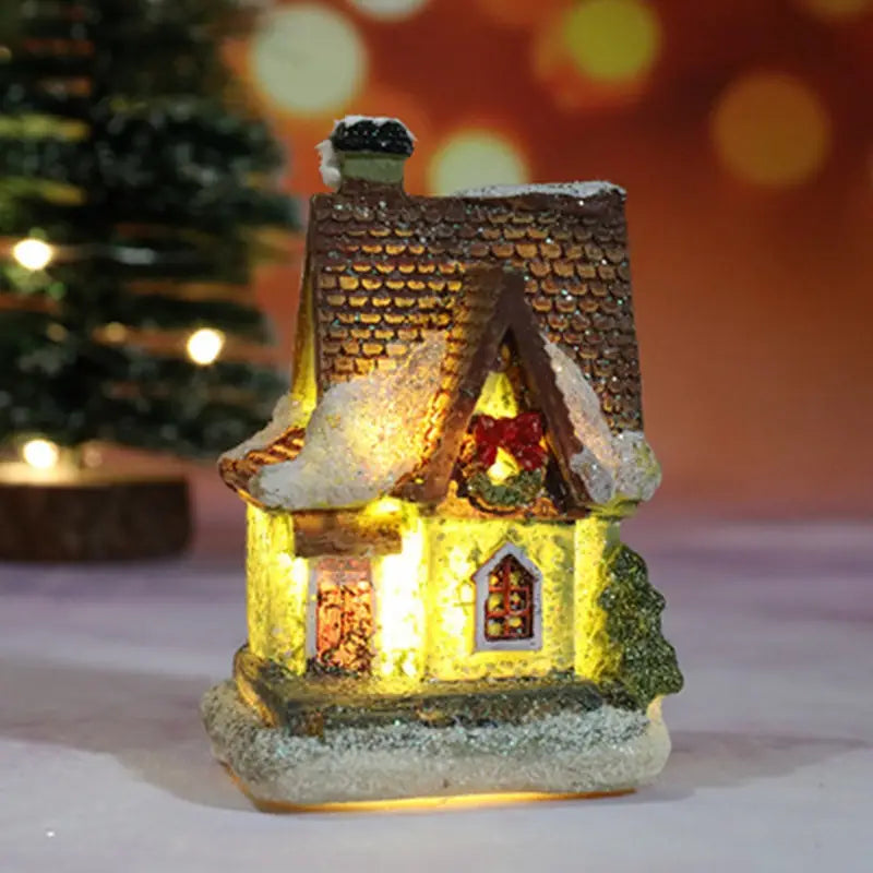 Une maison miniature du village de Noël à LED, illuminée, avec un toit en tuiles brunes et des détails blanchis par la neige, ainsi qu’un éclairage intérieur jaune chaud, veilleuse à batterie.