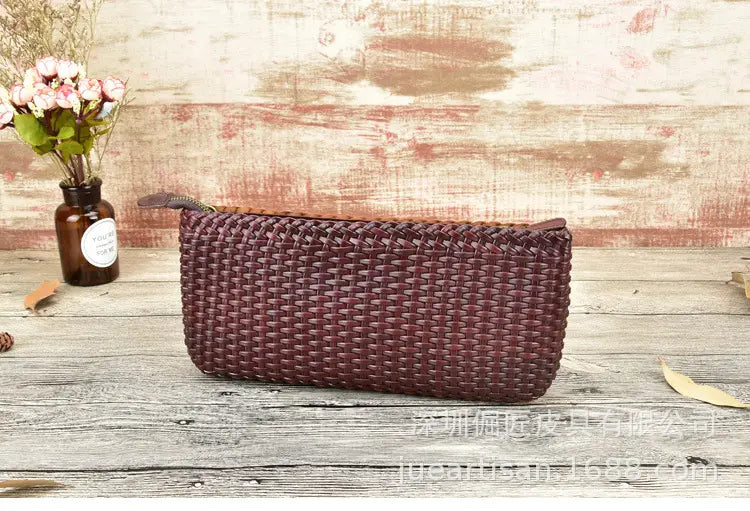 Un sac bandoulière en cuir véritable tressé bordeaux, présentant un design d’embrasse en peau de vache en couches avec fermeture éclair et une patte de tirage en forme de plume.