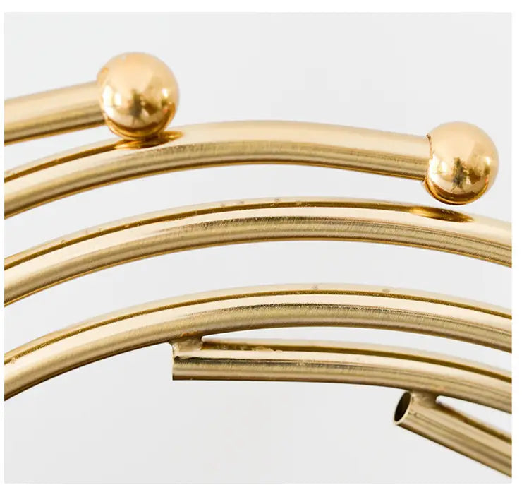 Gold-toned metal abstract sculpture featuring a wire rack with spherical finials at each end ideal for office desk decor.