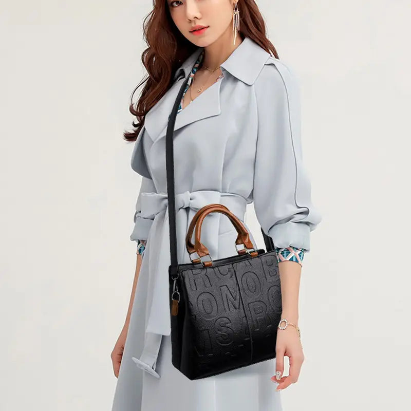 Black crossbody handbag style1 style2 crafted from pu leather featuring embossed lettering and brown leather handles in satchel style.