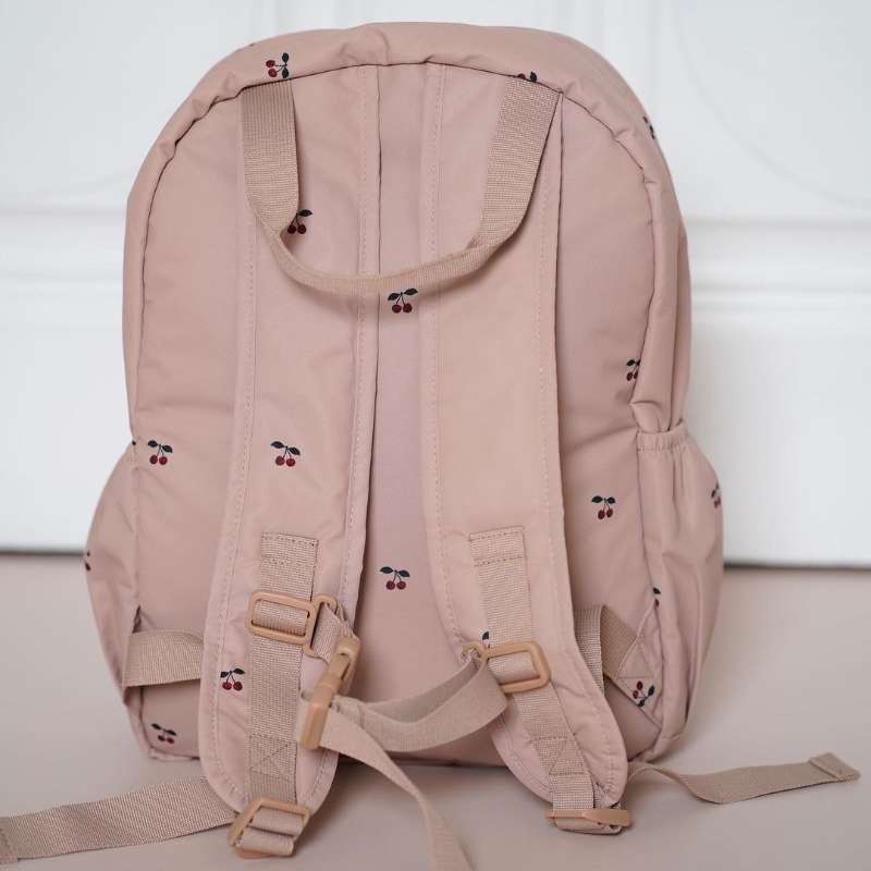 Ein weicher blush pinkfarbener gesteppten, bestickten Kinder-Rucksack mit zarter Kirschenstickerei, wasserfestem Stoff, verstellbaren Trägern und beigen Schnallen, entworfen als Schulrucksack.