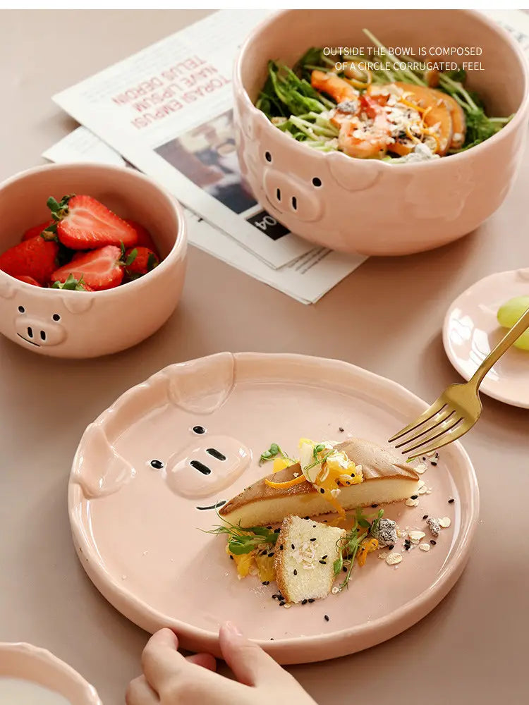 Cute pig ceramic dinnerware set featuring pink ceramic plate bowl and smaller bowl with molded facial features.
