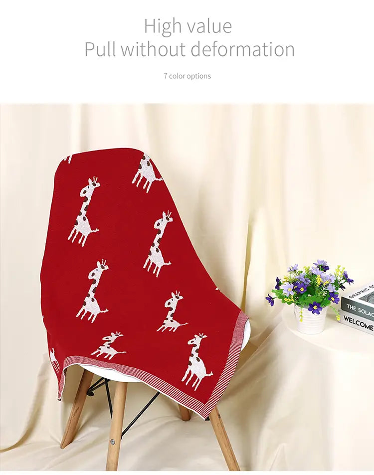 rote gestrickte Baumwoll-Babytdecke mit Giraffen aus Baumwolle mit weißen Giraffenmustern, über einen Stuhl drapiert