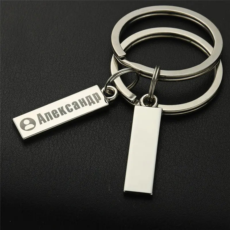 Silver rectangular personalized engraved metal anti-lost keychain with two dangling tags including one engraved with the name Александр and a profile icon.
