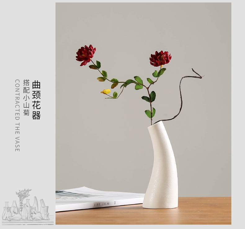 A modern white ceramic vase with a curved neck and tapered base holds two vibrant red flowers for floral decor.