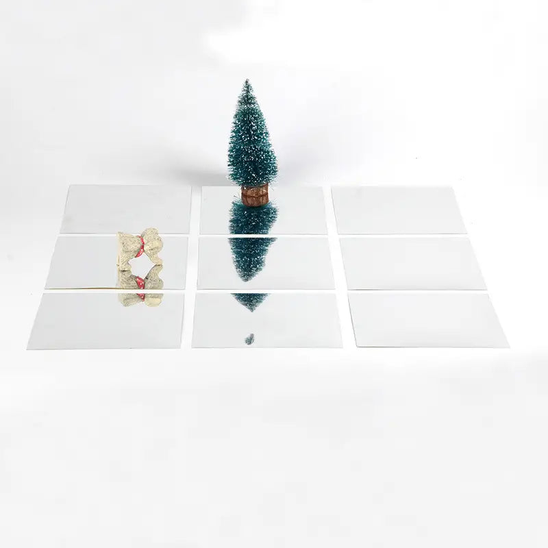 A miniature teal acrylic mirror wall sticker shaped like a Christmas tree with a brown base displayed on reflective mirror tiles for home living room and living room bedroom decor.