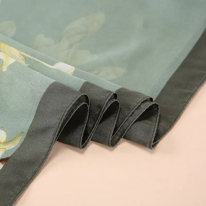 Un châle foulard en soie bleu clair délicat Van Gogh, amandiers en fleurs, présentant un motif floral subtil et une bordure satinée gris foncé.