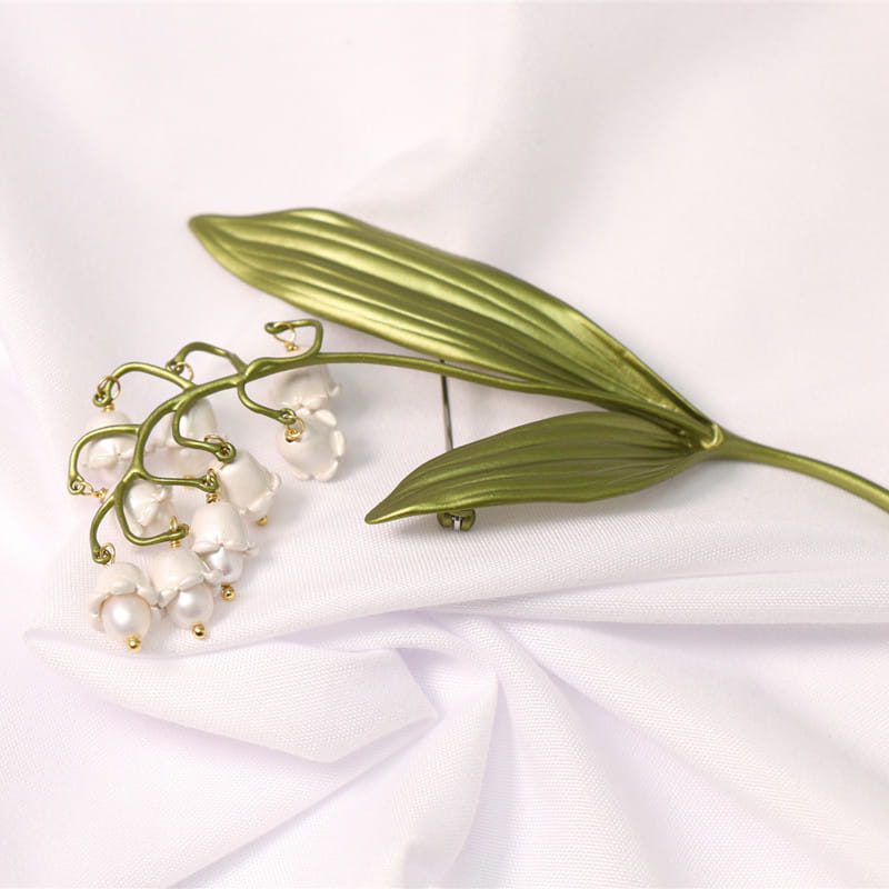 白い真珠のような花と緑の葉の茎を備えた、繊細な金色調の鈴蘭の真珠のブローチピン。