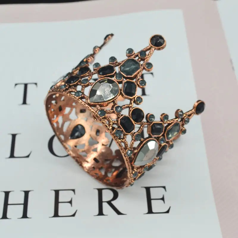 Ein Armband aus Roségold mit Mini-Kronen-Tortenaufsatz und Haar-Tiara, verziert mit schwarzen und klaren facettierten Edelsteinen.