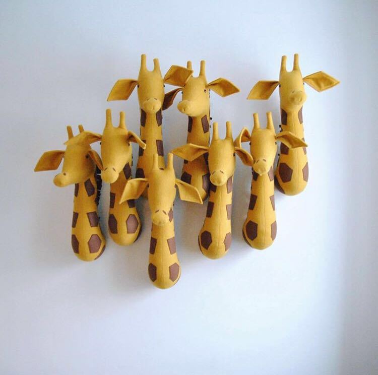 Eine Gruppe aus sieben handgefertigten gelben Giraffen-Wanddeko-Elementen aus Stoff mit braunen sechseckigen Flecken, im Stil einer 3D-Cartoon-Tierkopf-Wanddekoration