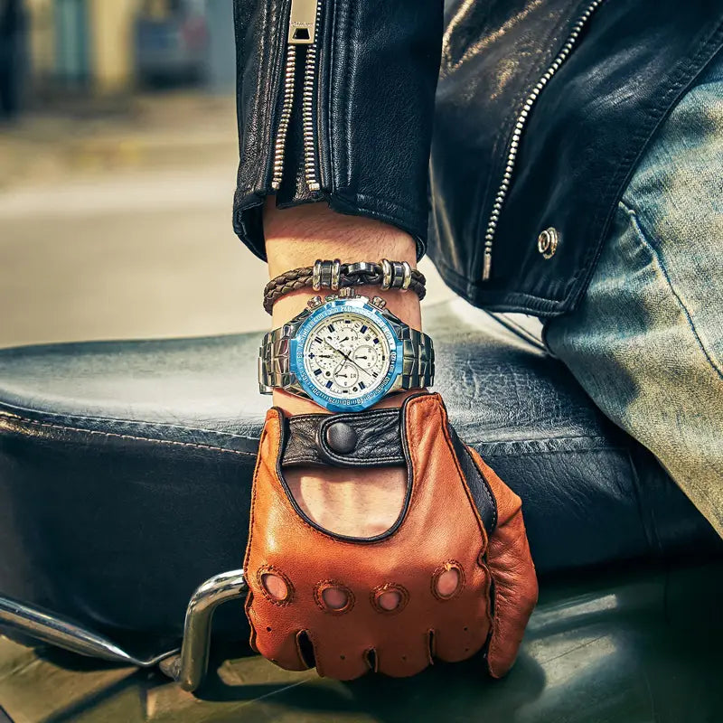 A bold blue and silver stainless steel gold chronograph watch for men with a white dial worn on a wrist covered by leather gloves.