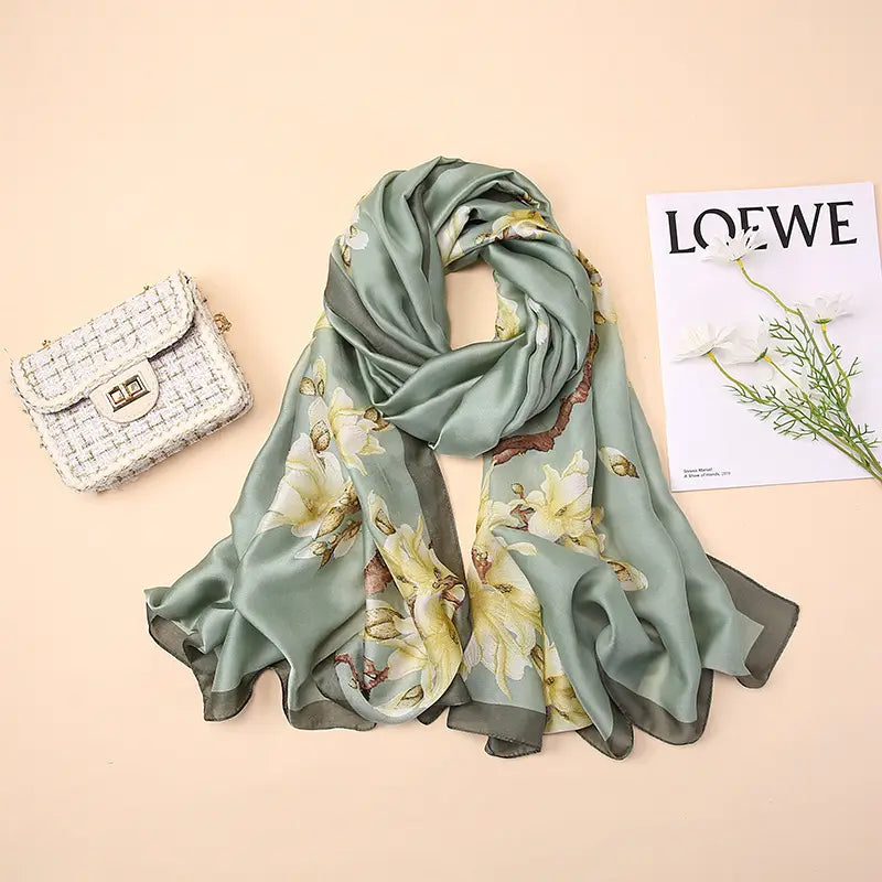 Un foulard châle en soie vert sauge souple présentant des motifs floraux délicats jaune et blanc, inspirés par les amandiers en fleurs de Van Gogh.