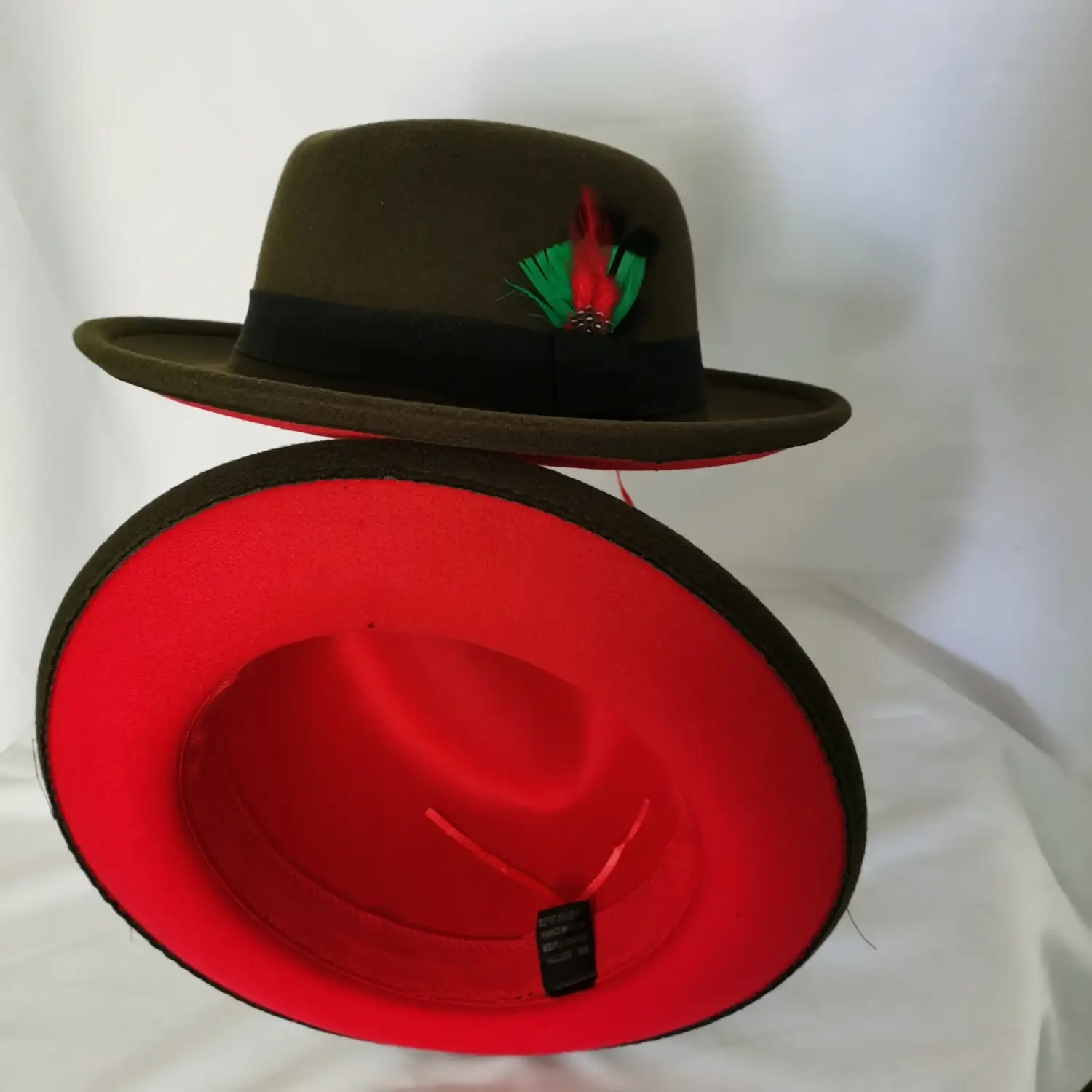 Unisex woolen felt fedora hat in olive green featuring a black band with a red feather accent and a vibrant red interior lining.