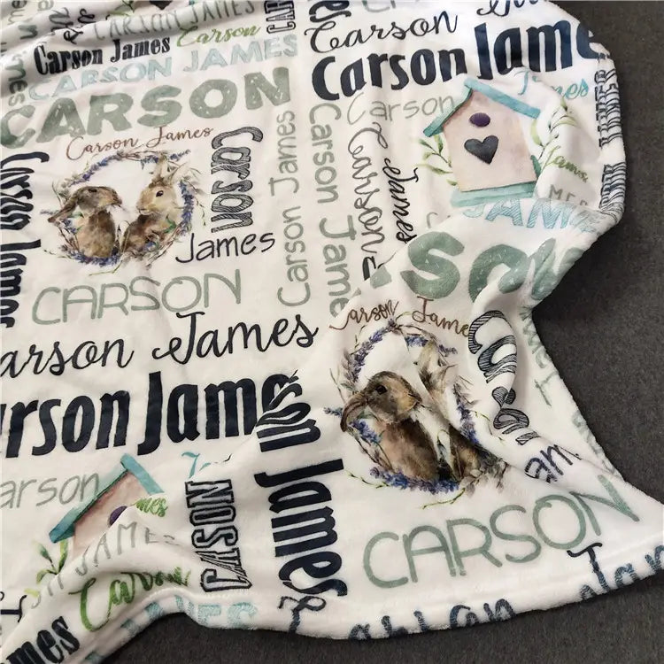 Personalisierte Baby-Wickeldecke aus Fleece für Neugeborene in weißem, plüschigem Material mit einem sich wiederholenden Muster des Namens carson james in verschiedenen Schriftarten und Farben, mit Illustrationen von Kaninchen und einem Vogelhaus.