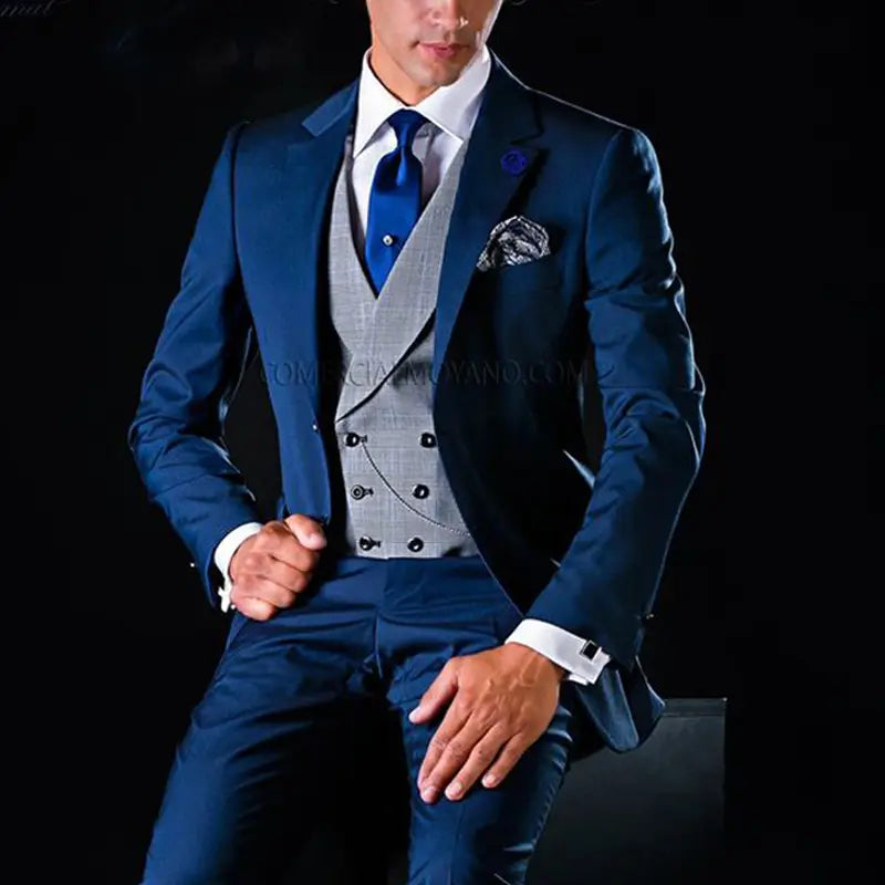 Un costume trois pièces pour hommes bleu marine, au tombé net, avec revers à encoches, met en valeur un gilet argenté à motif et un pantalon assorti, rehaussés d’une cravate bleu royal et d’un type de fermeture par bouton.