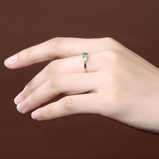 Ein Verlobungsring aus 18k Gold mit Smaragd und Diamanten: mit einem zarten Roségoldband, einem rechteckigen Smaragd-Zentralstein und zwei kleinen Diamanten jeweils seitlich.