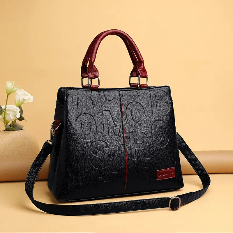 Black crossbody handbag style1 style2 crafted from black pu leather with embossed lettering and contrasting burgundy handles and strap.