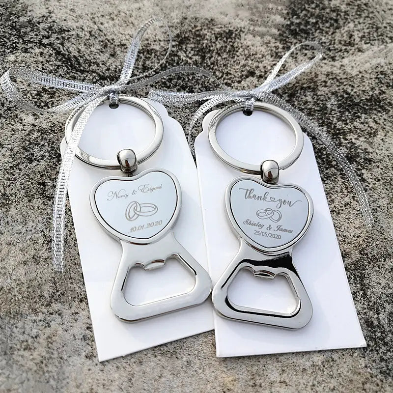 Porte-clés décapsuleurs en métal argenté en forme de cœur gravés des détails du mariage et anneaux attachés à l’aide d’un ruban argenté, pour des faveurs de mariage personnalisées en décapsuleur en forme de cœur.