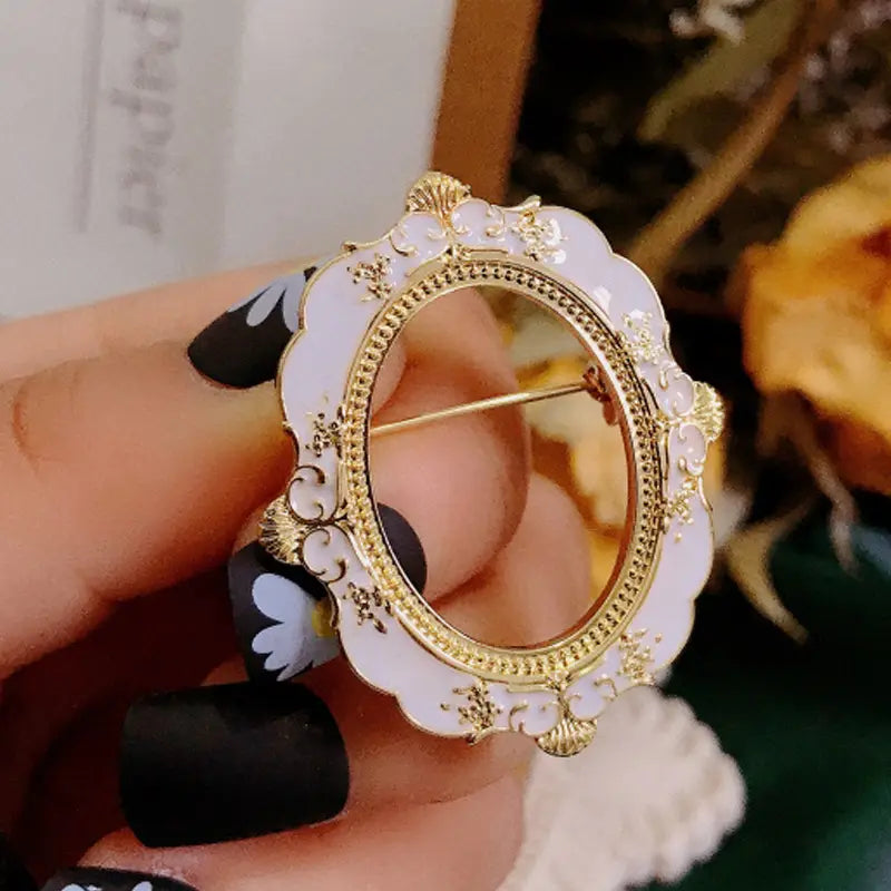 Broche para marco de cuadro con arte de David barroco, ovalado y ornamentado, con marco de esmalte blanco y detalles en metal con acabado tono dorado, que incorpora delicados motivos florales a lo largo de los bordes festoneados.