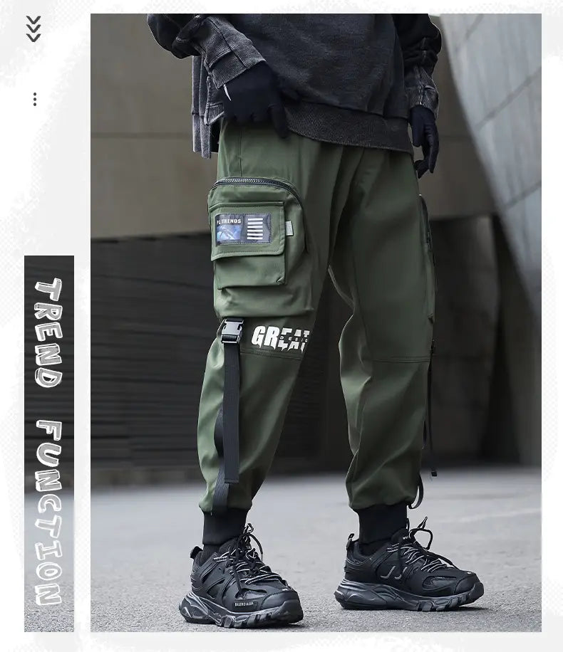 Herren schwarze taktische Cargo-Jogginghosen im Streetwear-Stil mit olivgrüner Cargo-Hose mit mehreren Taschen, Detail mit Seitenriemen und weißem Schriftzug am Bein.